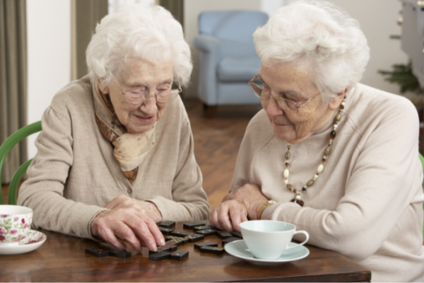 Older women wearing glasses, playing dominoes and drinking tea