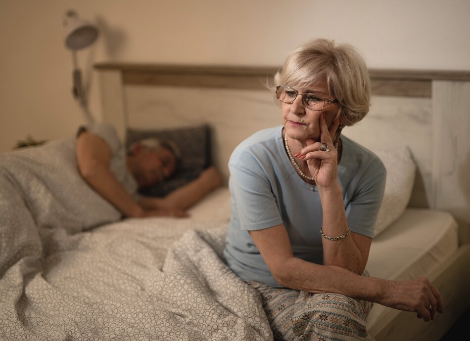 Woman sitting on edge of bed while partner sleeps