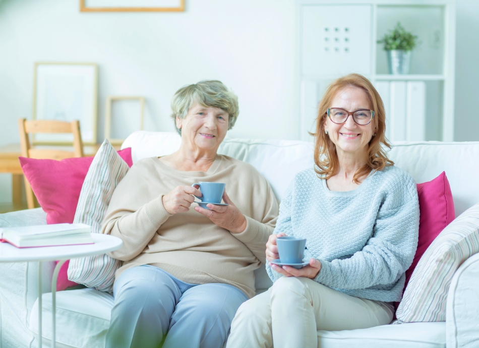 Mother and daughter with cups of tea smiling at camera 