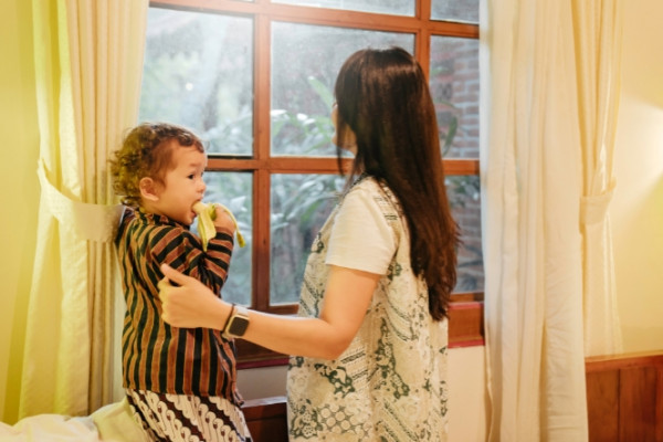 Woman with child looking out through bedroom window