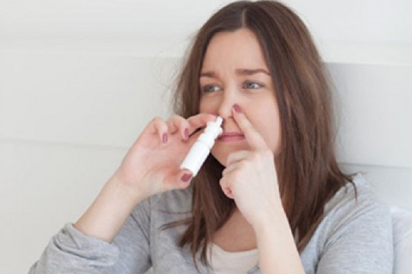 Woman using nasal spray in one nostril and blocking the other