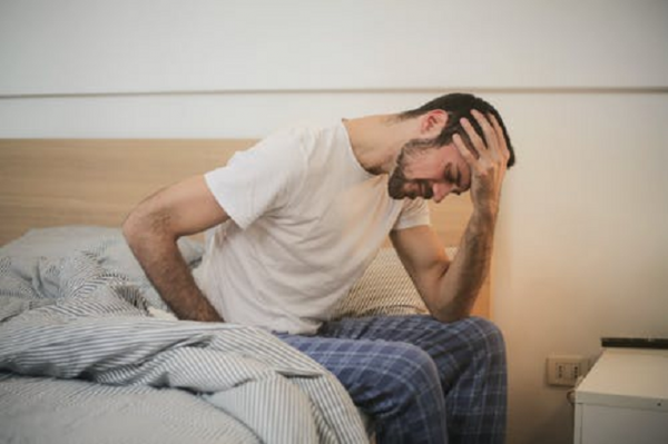 Man sits on side of bed with head in hands, worried