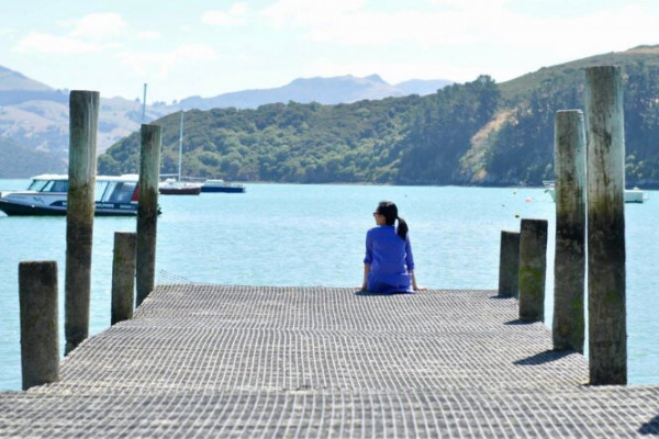 Woman sits at end of wharf looking to lake