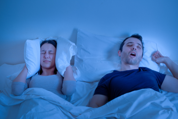 Man snores while woman puts pillow over her ears