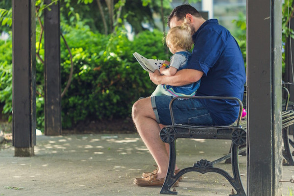Dad sitting on park bench reading to toddler