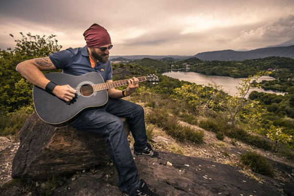 Man playing a guitar on top of hill overlooking lake