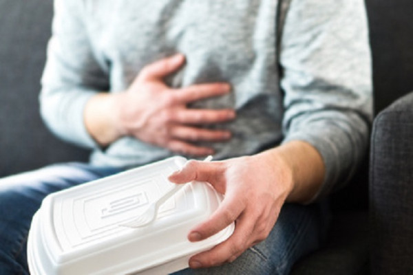 Man holding takeaway food container has stomach pain