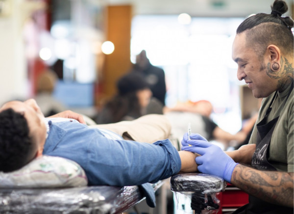 Māori tattoo artist at work talks to customer