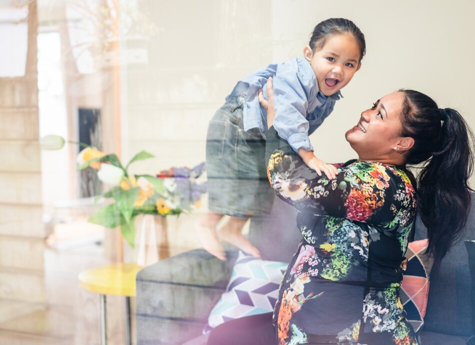 Happy Māori mum holds young daughter up in the air