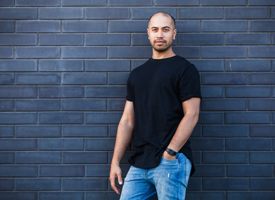 Young Maori man posing against grey brick wall 