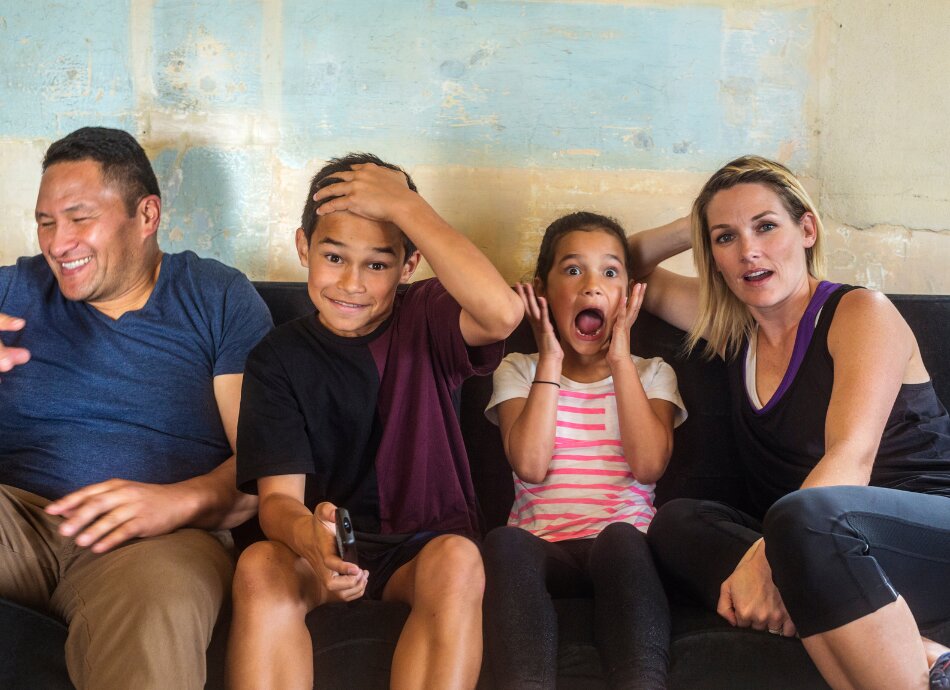 Mixed race New Zealand family of 4 laughing on couch