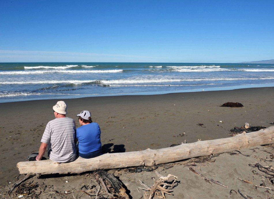 2 people sit on a log at Christchurch NZ beach