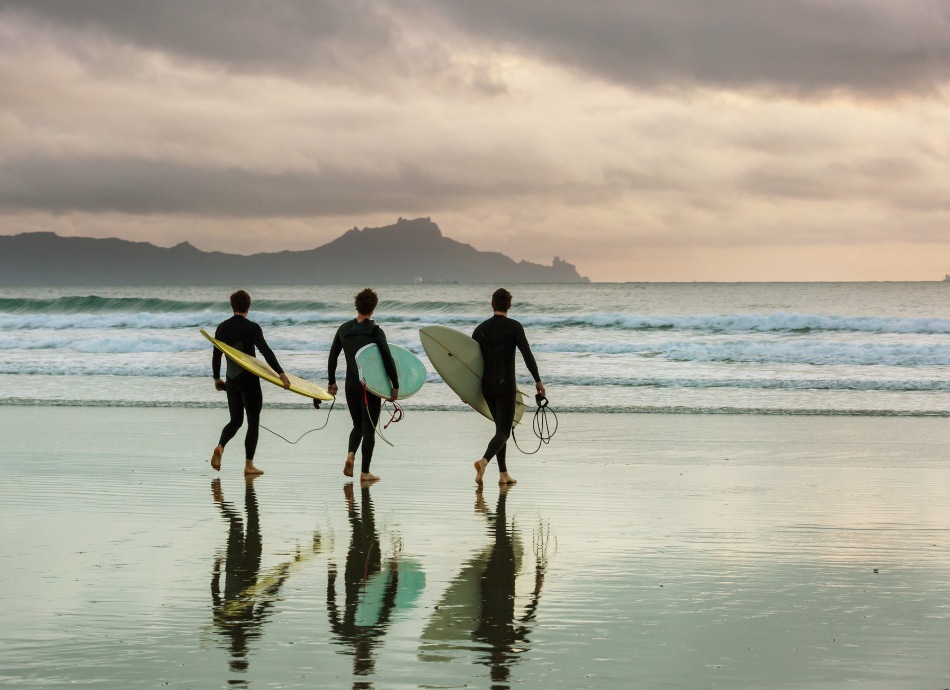 3 surfers walk into the surf on New Zealand beach
