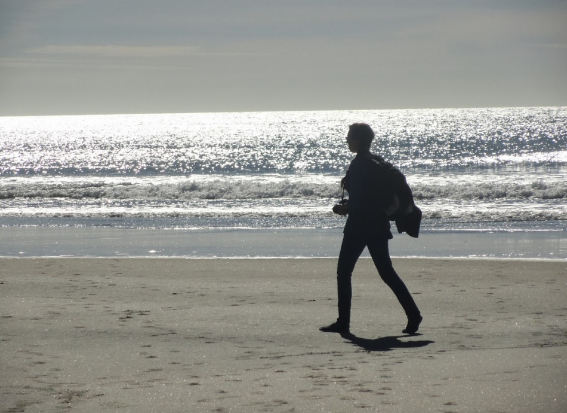 Woman silhouetted walking on beach in NZ HN 950x690
