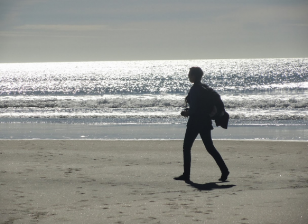 Silhouetted woman walking along sandy beach waterline