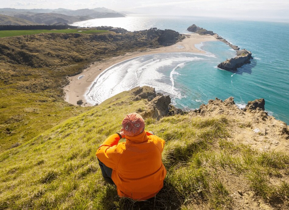 Woman in orange sitting on a hilltop in New Zealand