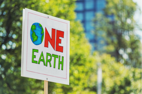 Placard saying one earth with trees and a building behind