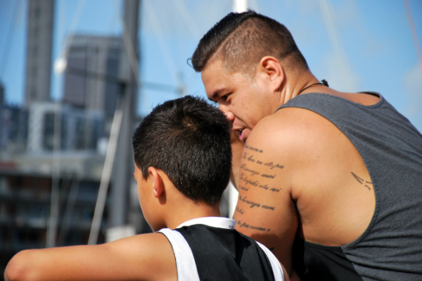Pasifika man and son leaning on railing at the harbour